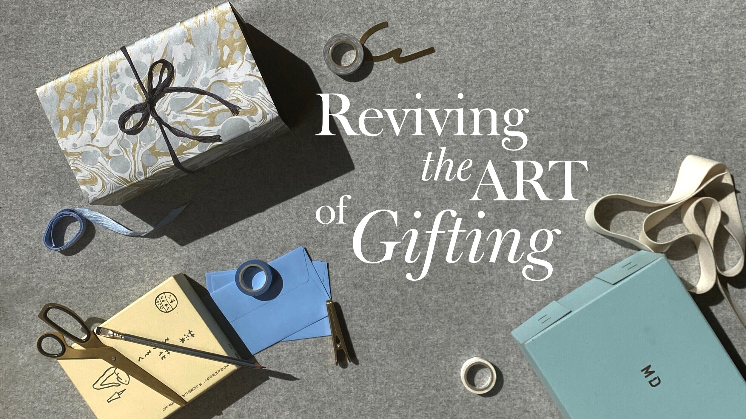 A gift wrapped in silver and gold paper, with a bow, sits next to ribbon, scissors and tape.