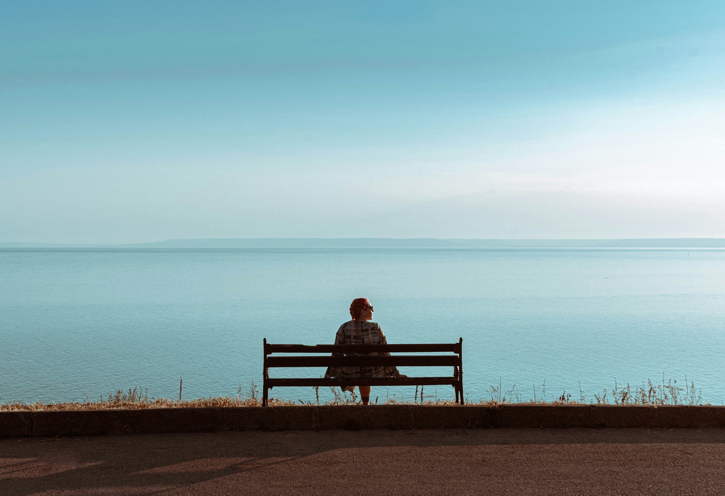 Woman sitting on a bench in front of peaceful lake.