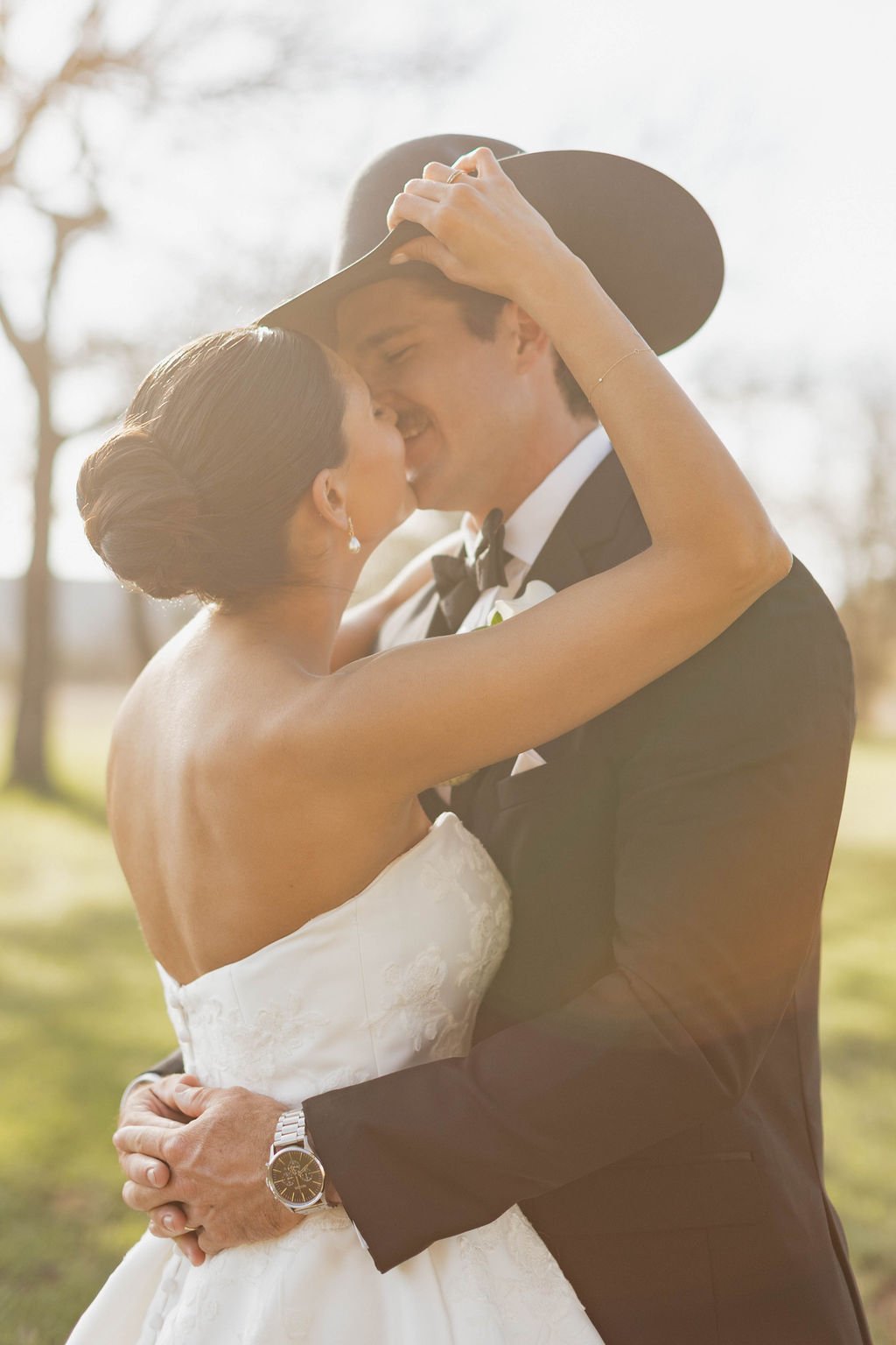 Cowboy black tie wedding with the bride taking off the grooms hat for a kiss.