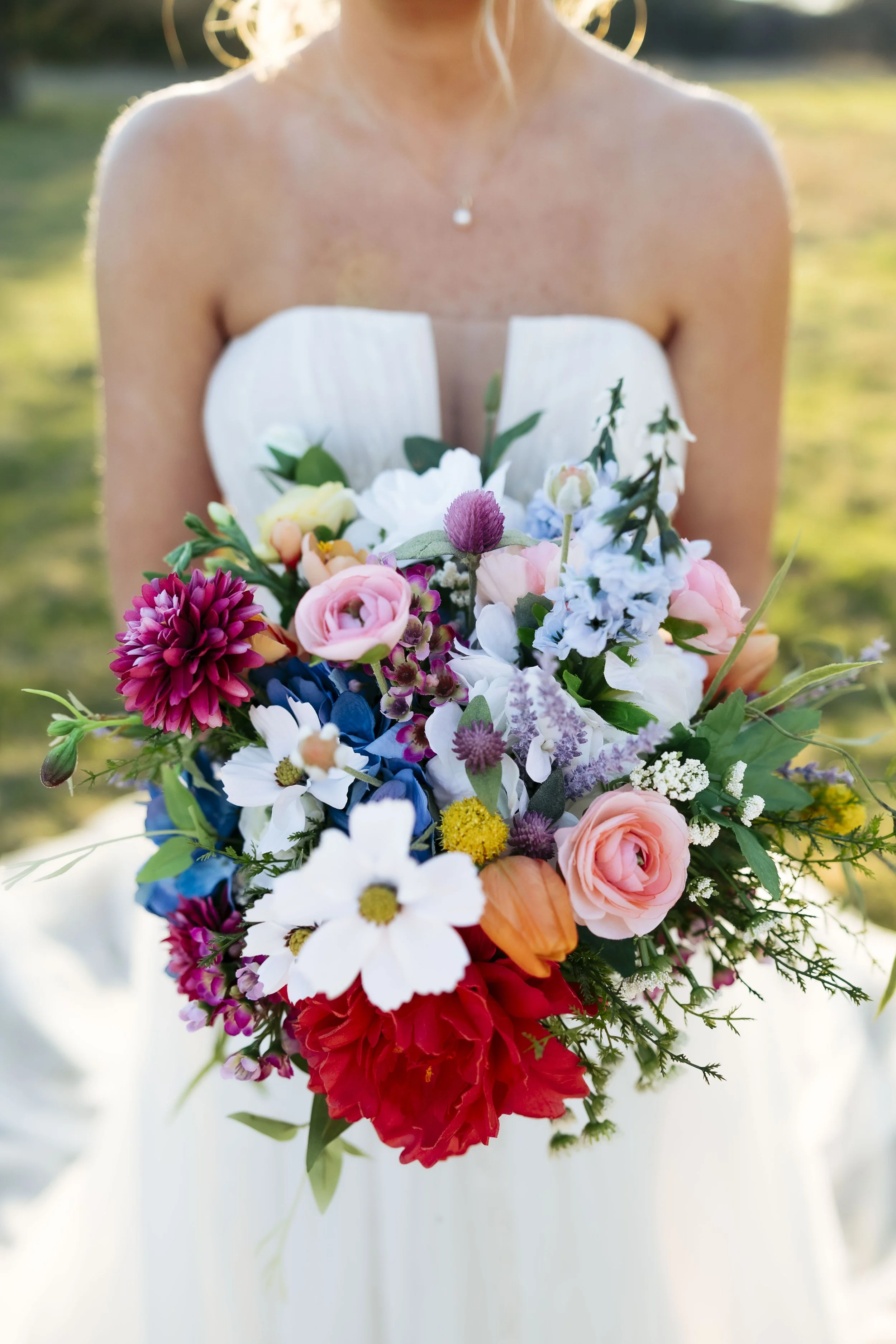 Up close photo of spring bridal bouquet with a mix of so many colors it's very unique. It's a true spring mix of whimsey with large and small flowers, blues, purples, pink, white, and red, and peach. Perfect for a spring ranch bride.