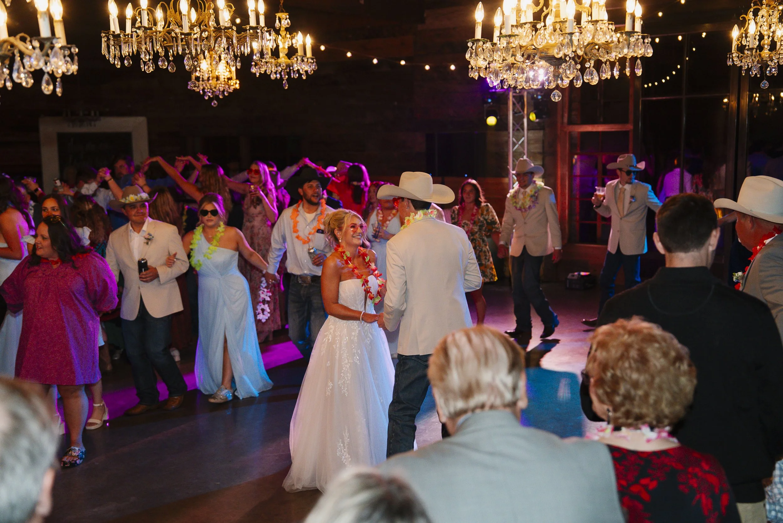 Photo of groom and bride in the middle of the dance floor packed with guests dancing and cool lighitng from the DJ making the chandeliers sparkle. This dance floor was first the ceremony space due to rain plan.