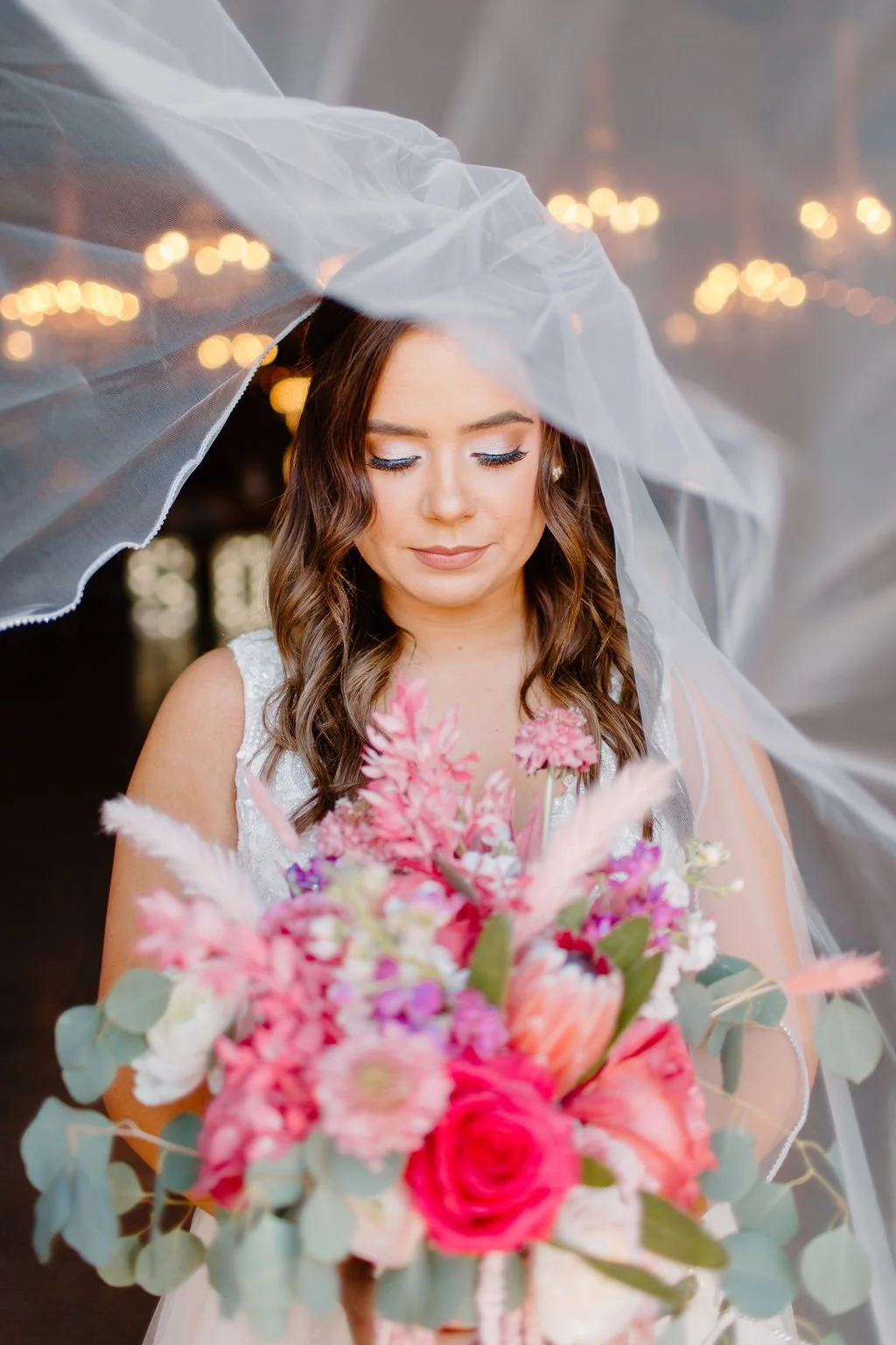 Bride looking down at bouquet of pink flowers in barn north texas wedding