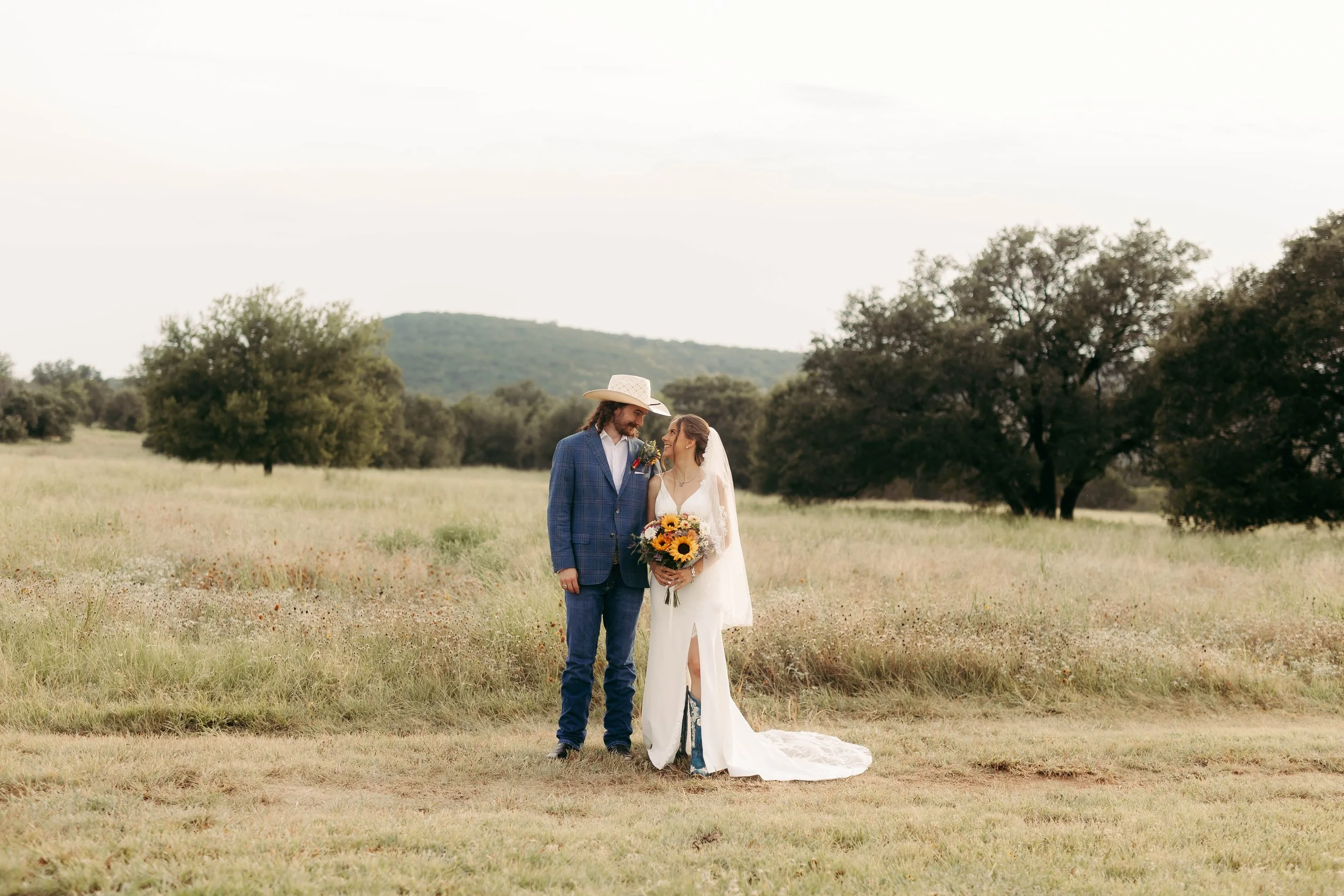 Couple taking portrait photos after the wedding on a ranch in North Texas with wildflowers and rolling hills in the backdrop.