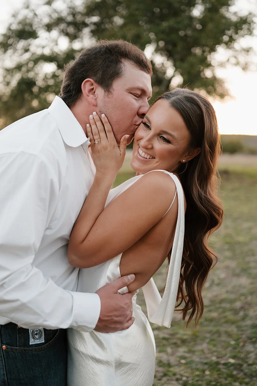 Chic bride in silk gown being kissed by her cowboy husband on wedding day where both rustic and chic came together.