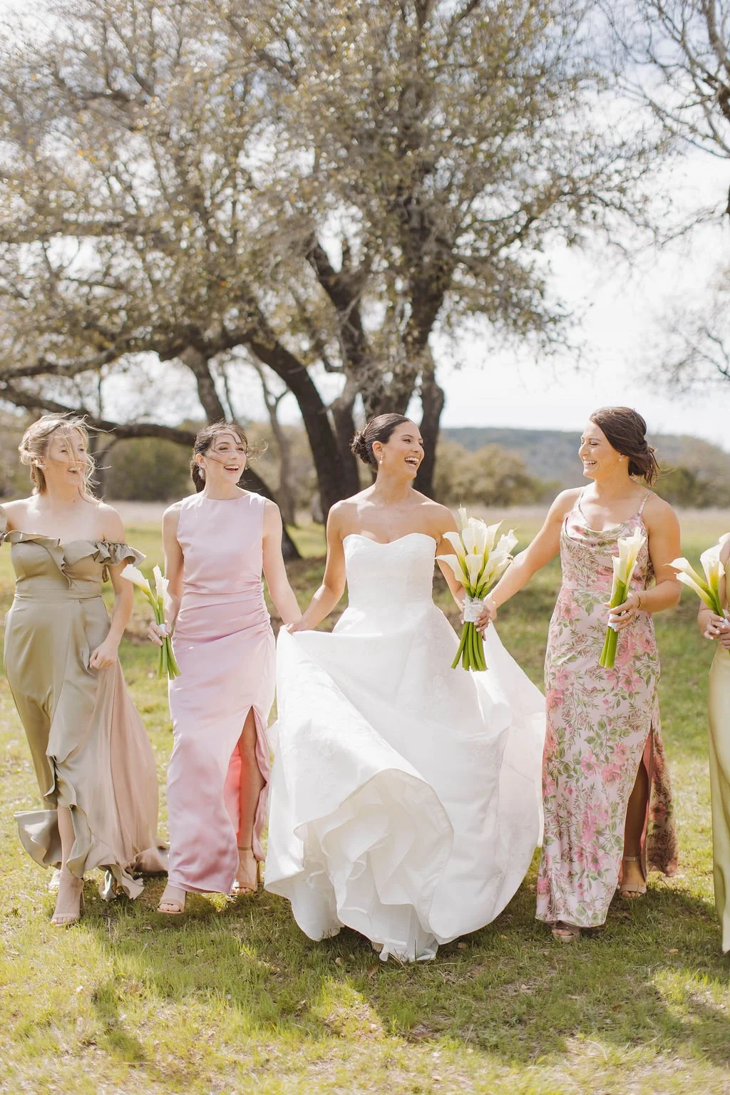 Spring bride with sleek bun and lily bouquet with bridesmaids in their mix matching spring floral dresses.