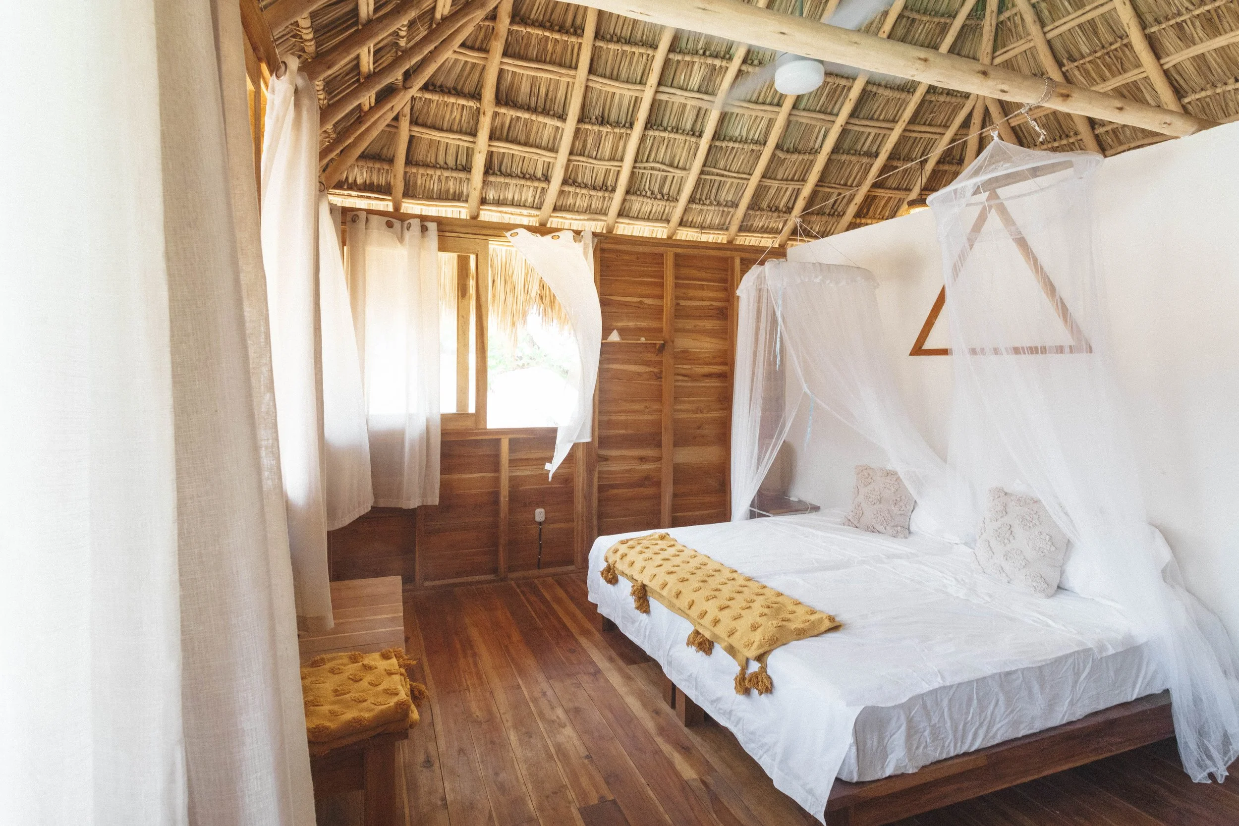 Upstairs cabaña room with a mosquito-net canopy bed and thatched roof at Still Salty Escape in Nicaragua