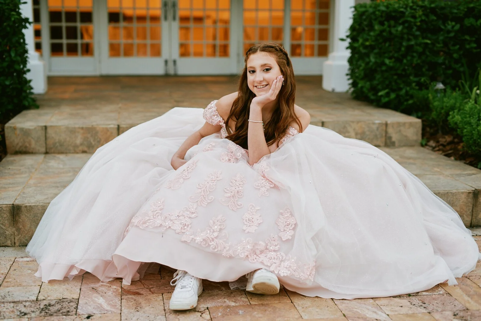 Young woman in a pink wedding dress sitting on outdoor stone steps.
