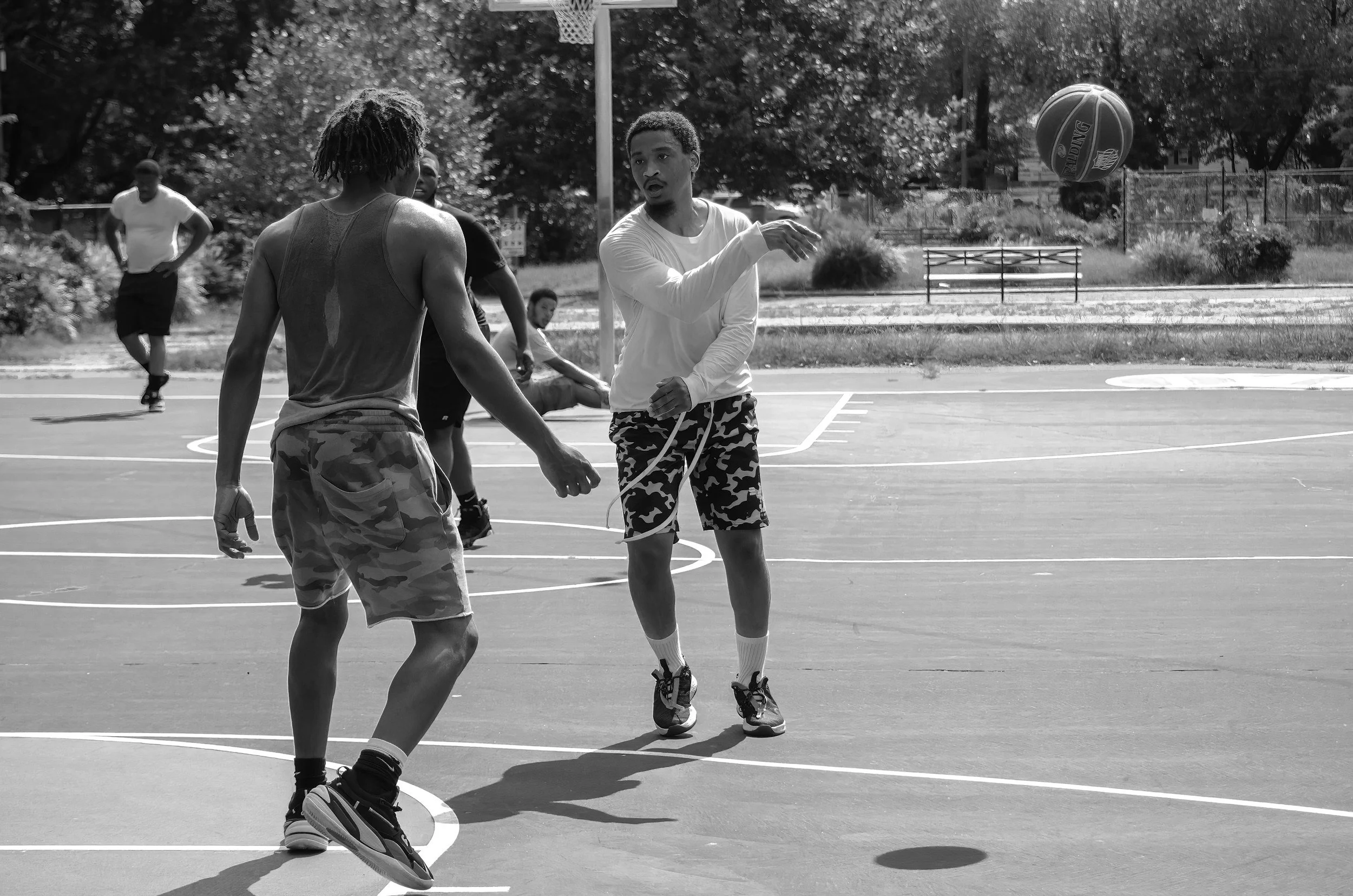 A black-and-white photograph of friends playing basketball on an outdoor court.