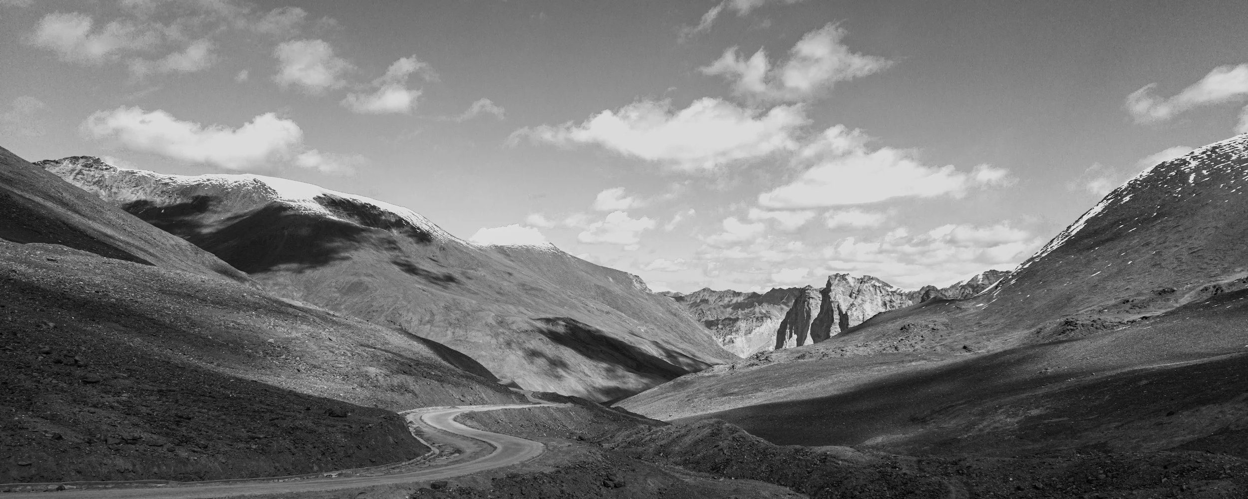 A winding path through an open mountain valley in black and white.