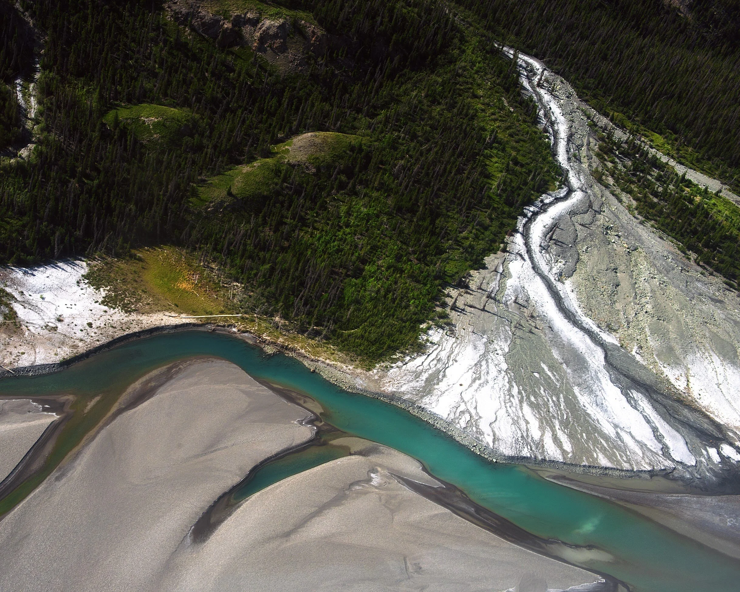 Aerial view of a winding river flowing through a mountainous landscape with dense evergreen forest and sandbars Yukon, Canada.