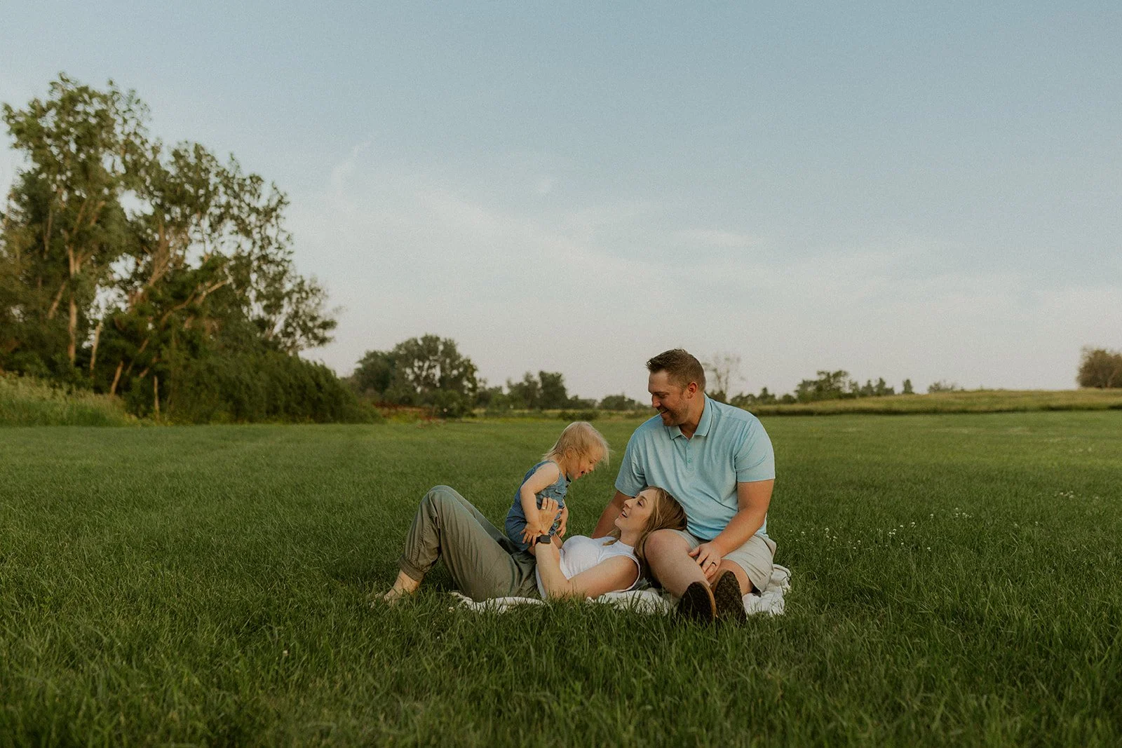 Scenic landscape with mountainous hills, a lake, and grassy plains in the foreground under a cloudy sky.