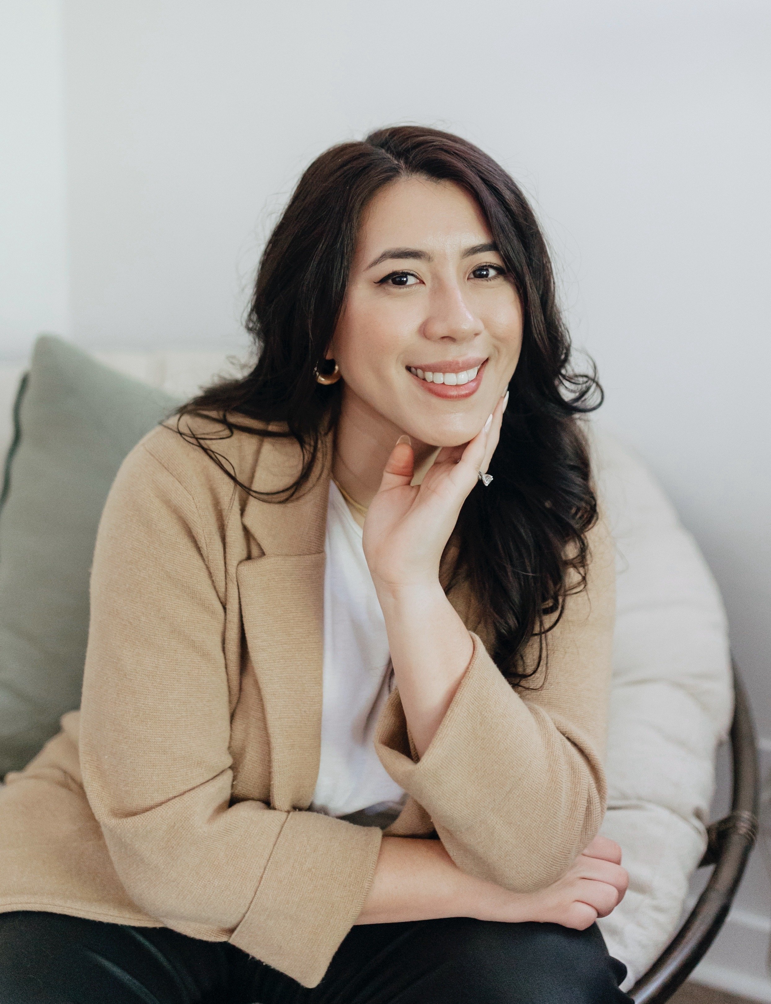 Person smiling, wearing a beige blazer, sitting indoors.