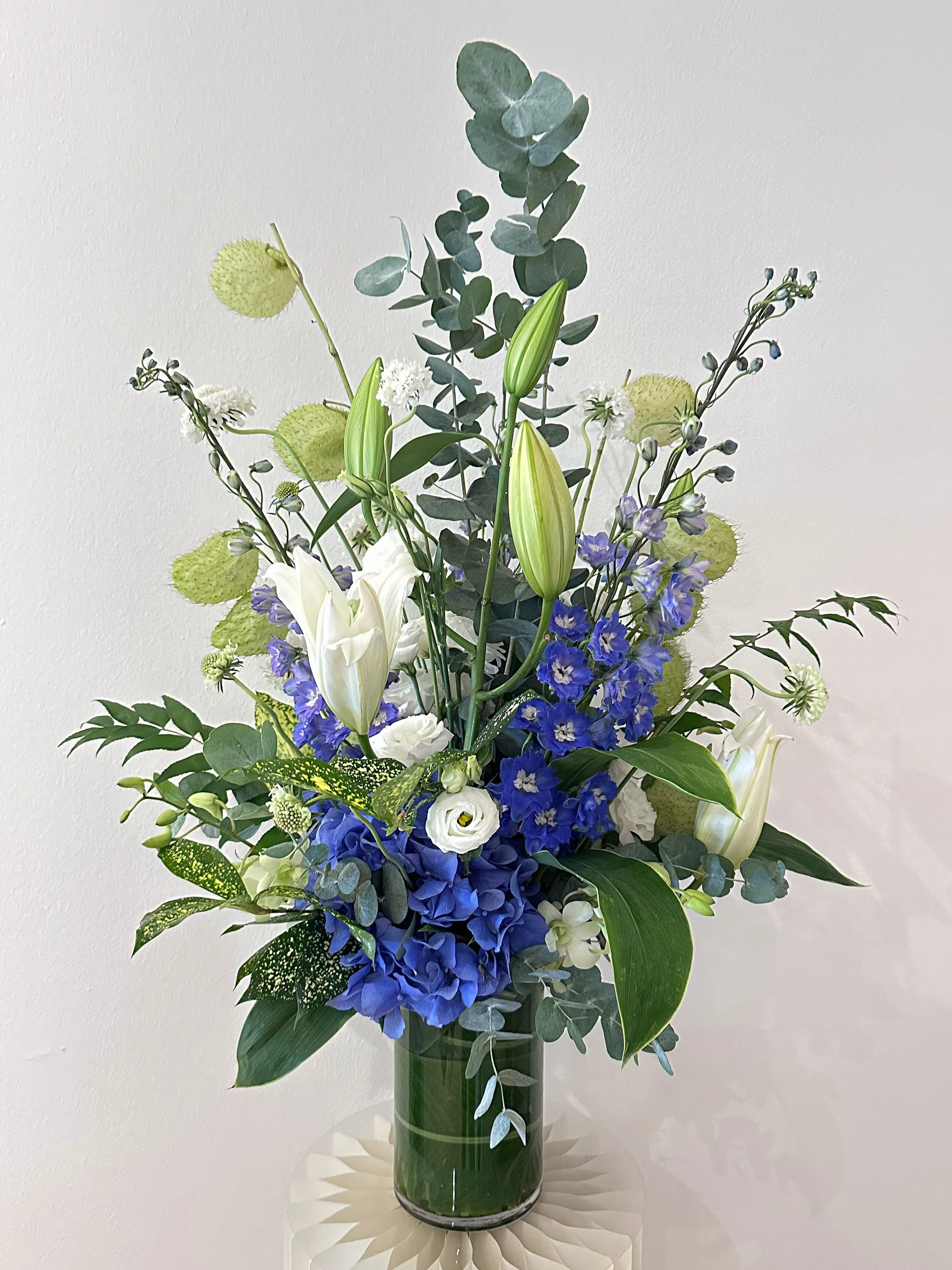 Blue hydrangea, white oriental lily, delphinium in that particular shade of violet-blue that&rsquo;s hard to name and harder to forget.

This arrangement is part of a standing subscription &mdash; flowers delivered to the same home, every week, witho