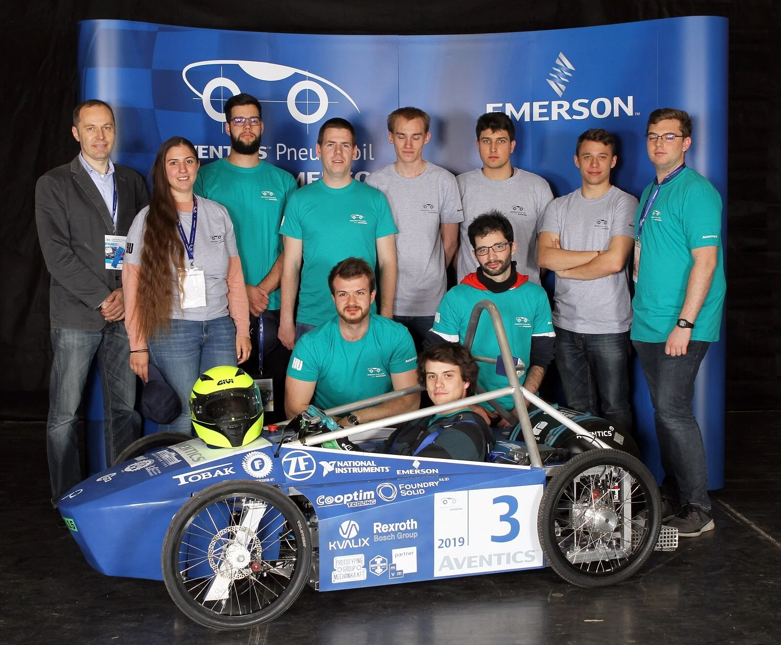 Photo: Ádám Detzky sits in the Budapest University of Technology and Economics winning vehicle with teammates Milán Bolgár and Máté Szentes behind him. Standing from left to right are Dr. Zsolt Farkas, Réka Tobak, Zsolt Németh, Tamás Szlobodnik, Zol…
