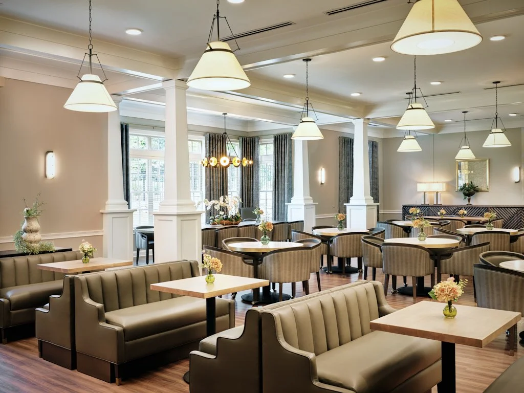 Modern restaurant interior with booths and round tables, pendant lighting, and floral centerpieces.