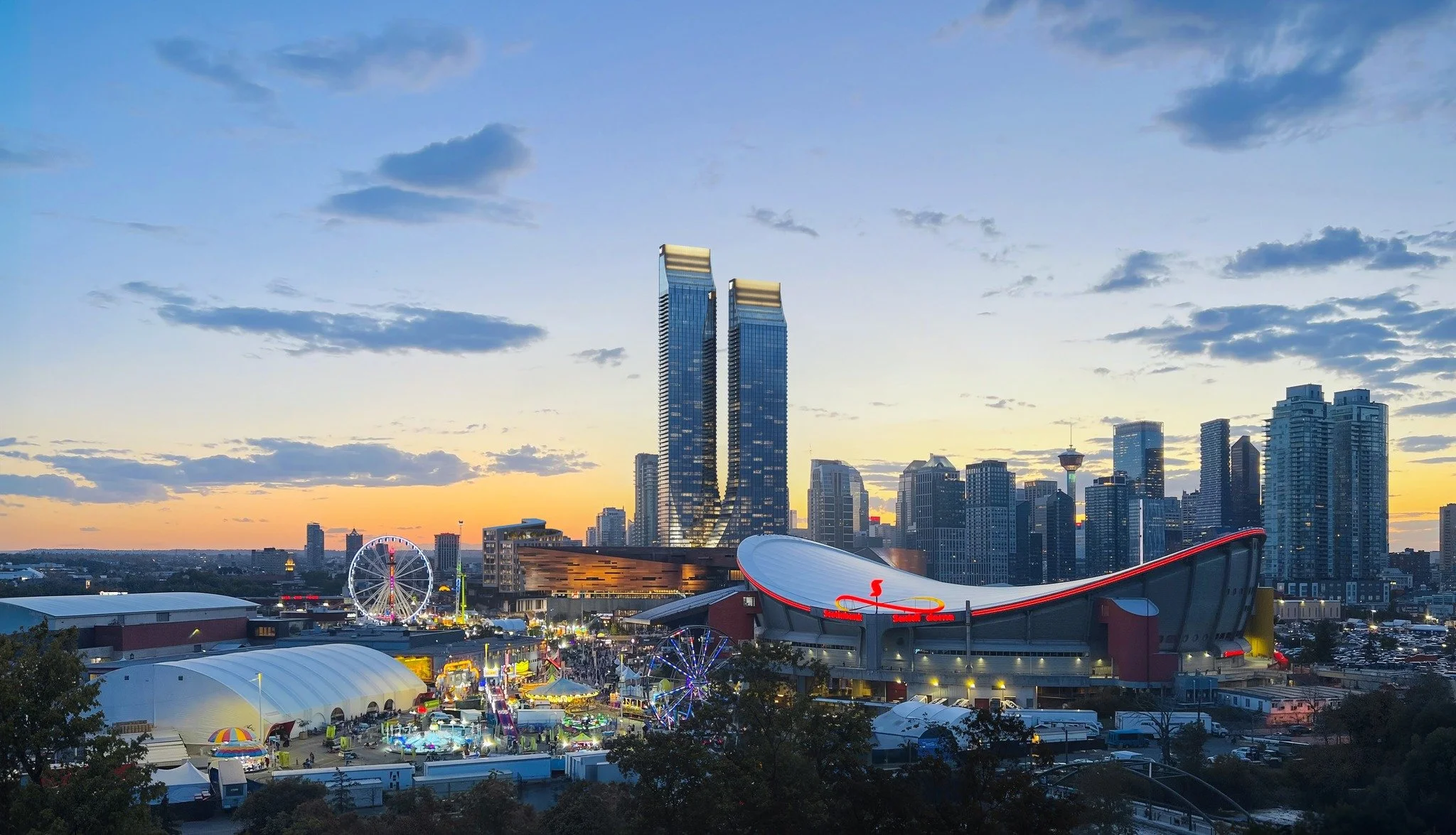 Photo rendering of Calgary's Culture + Entertainment District with the W & JW Hotel and Residences against the city skyline in the background and the Saddledome, Calgary Stampede midway and BMO Centre in the foreground.