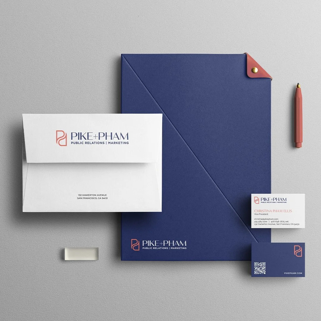 Business stationery including an envelope, business card, notebook, and pen with Pike + Pham branding on a gray surface.