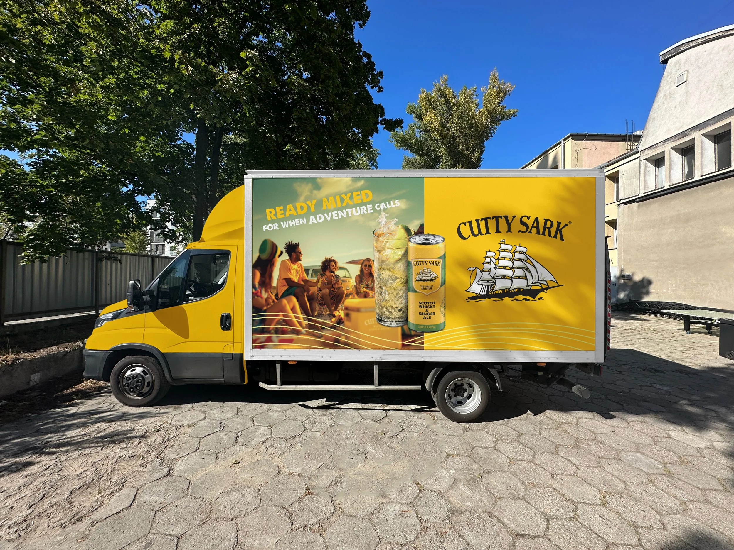 A yellow delivery truck with an advertisement for Cutty Sark whiskey and a picture of friends enjoying drinks outdoors.