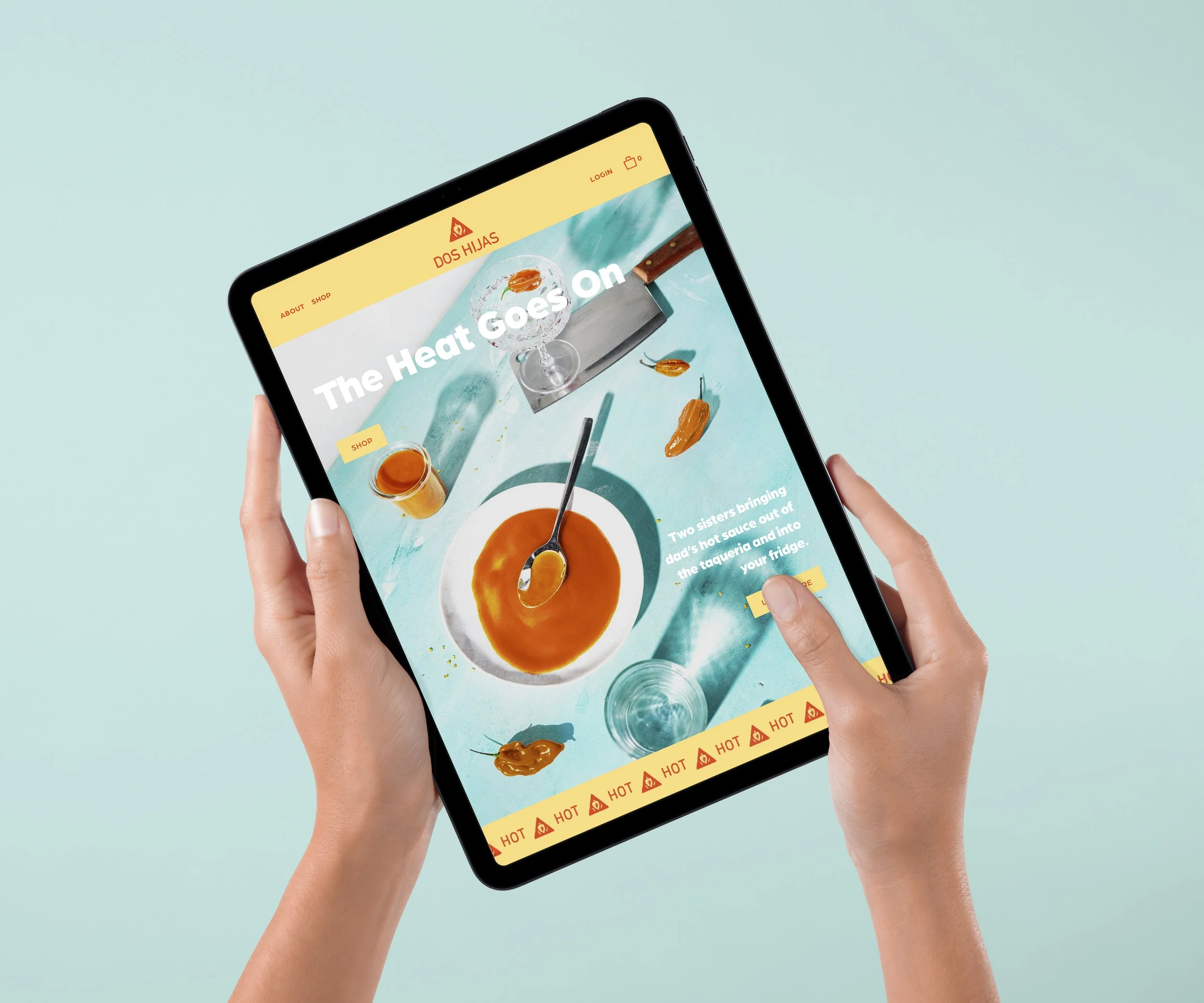 A person holding a digital tablet displaying a website with a bowl of hot sauce, chili peppers, and a glass of water on a light blue background.