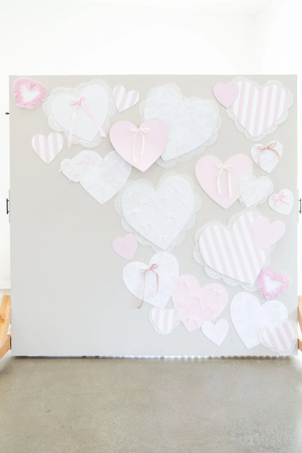 Decorative display of pink and white paper hearts with lace borders and ribbons on a white wall panel.