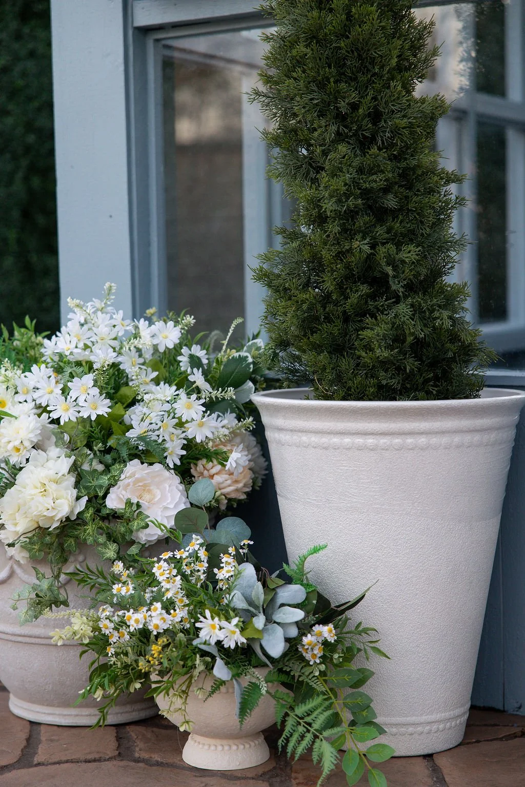 Potted Christmas tree with white flowers and greenery on a porch.