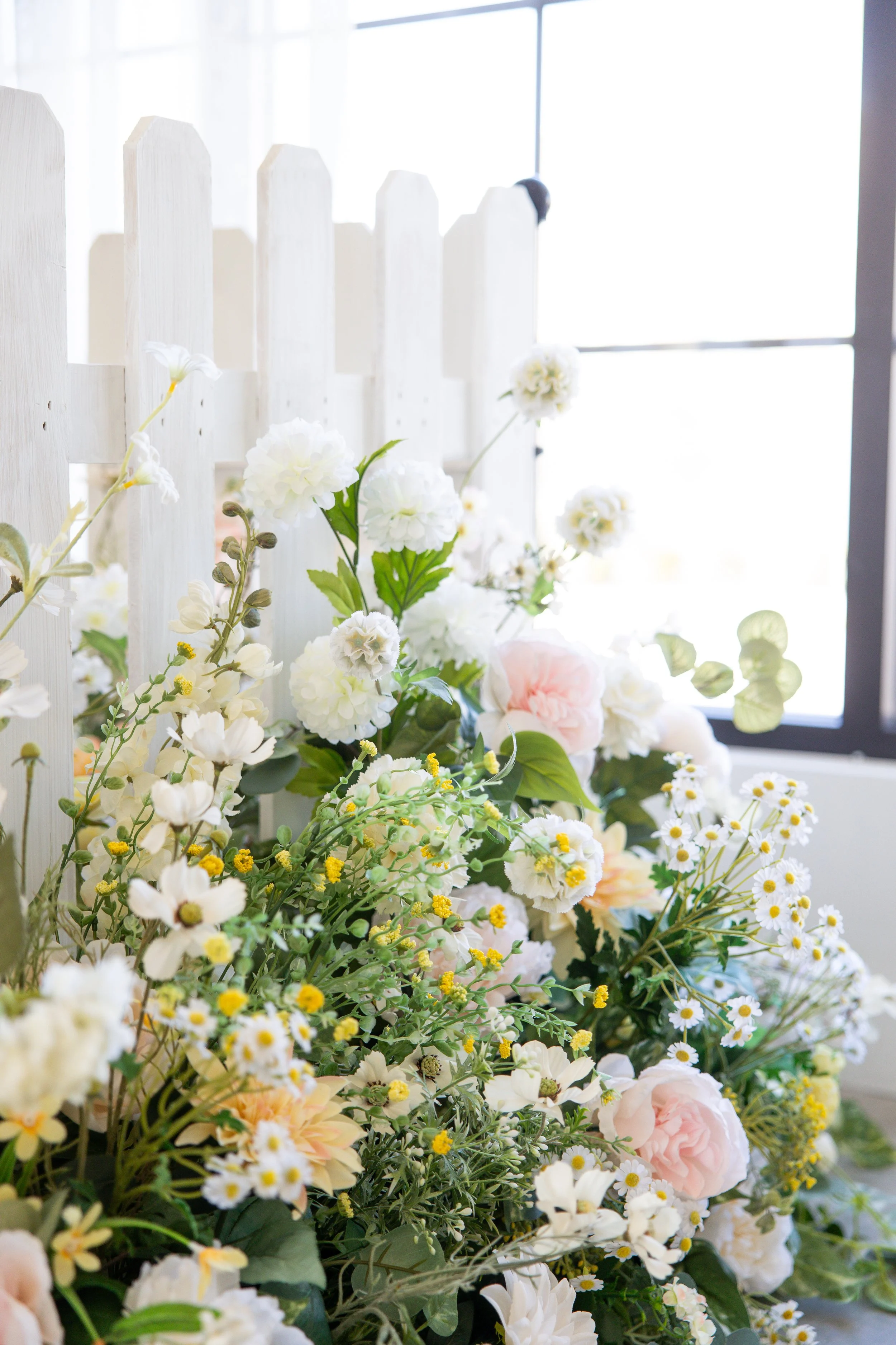 A white chair with decorative backrest and gold legs, on a light pink rug, sits in front of a pink curtain backdrop tied in bows.