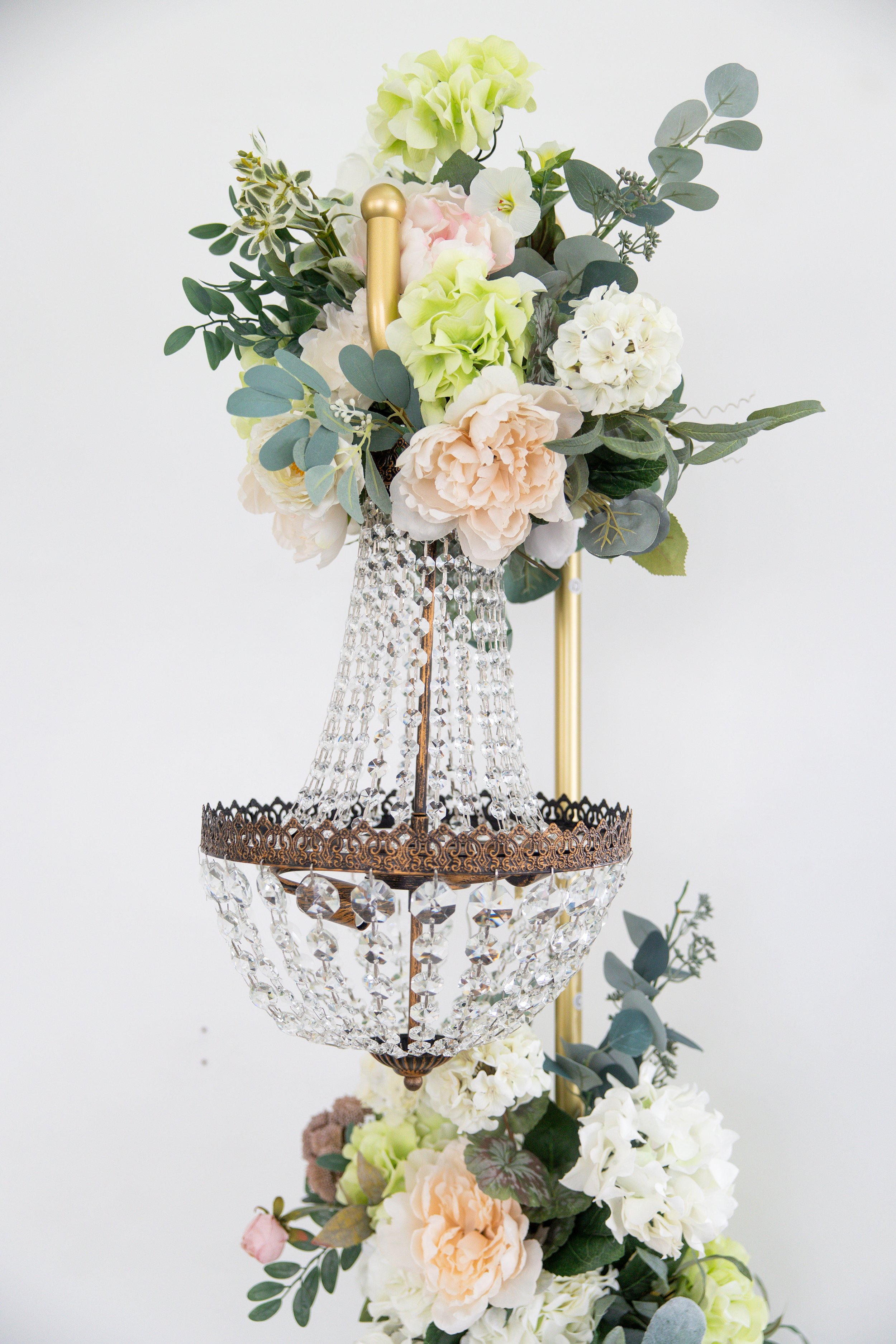 A green vintage-style sofa with gold legs in front of a large light gray wall and white background, with sunlight streaming in from the left.