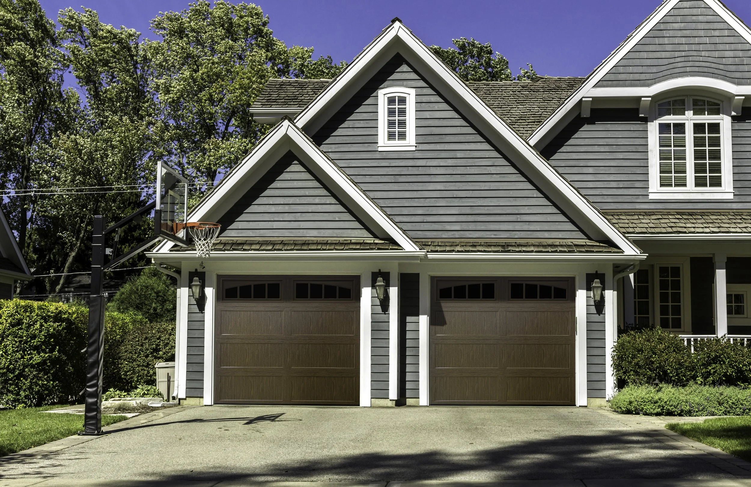 Exterior view of a house with gray siding, brown garage doors, and a basketball hoop in the driveway.