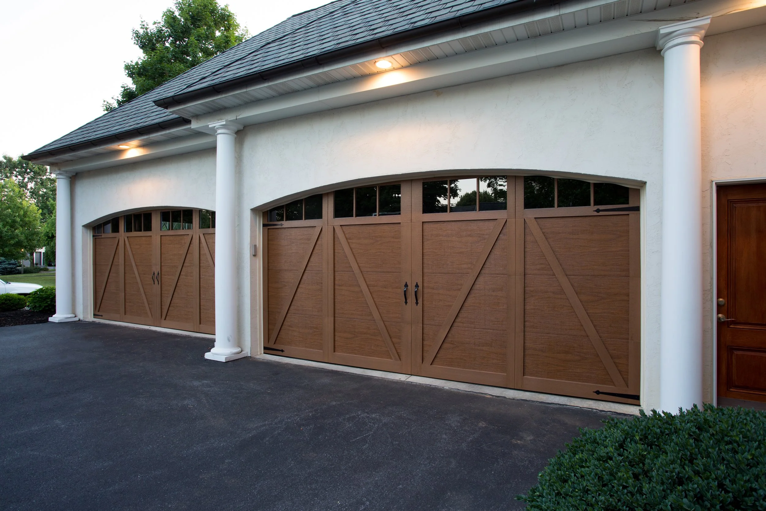A house with a white exterior, grey roof, white columns, and two brown wooden garage doors.