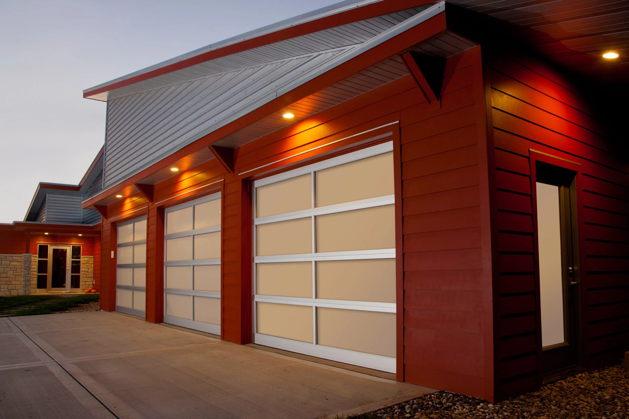 Modern house with red siding, two large garage doors, and exterior lighting at dusk.