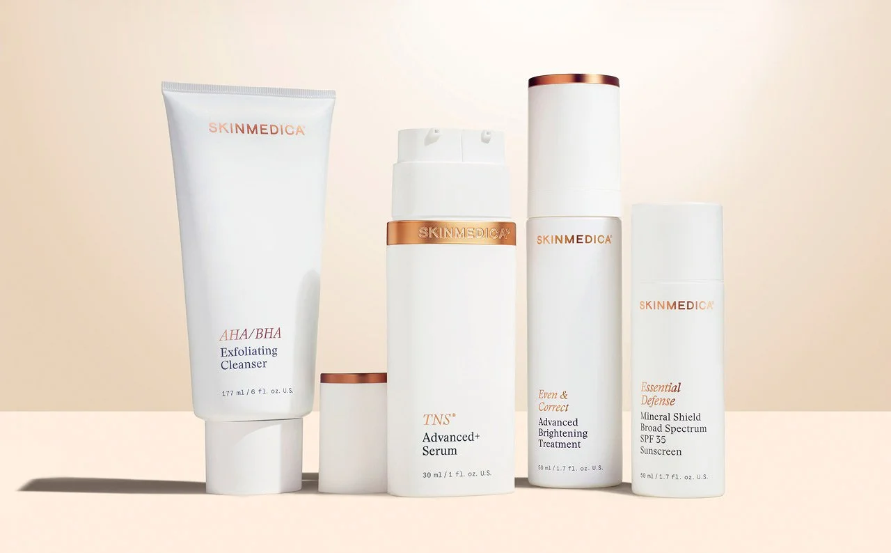 four SkinMedica products with new, lab coat white packaging. Showcasing AHA/BHA Exfoliating Cleanser, TNS A+, Even and correct advanced serum and essential defense SPF