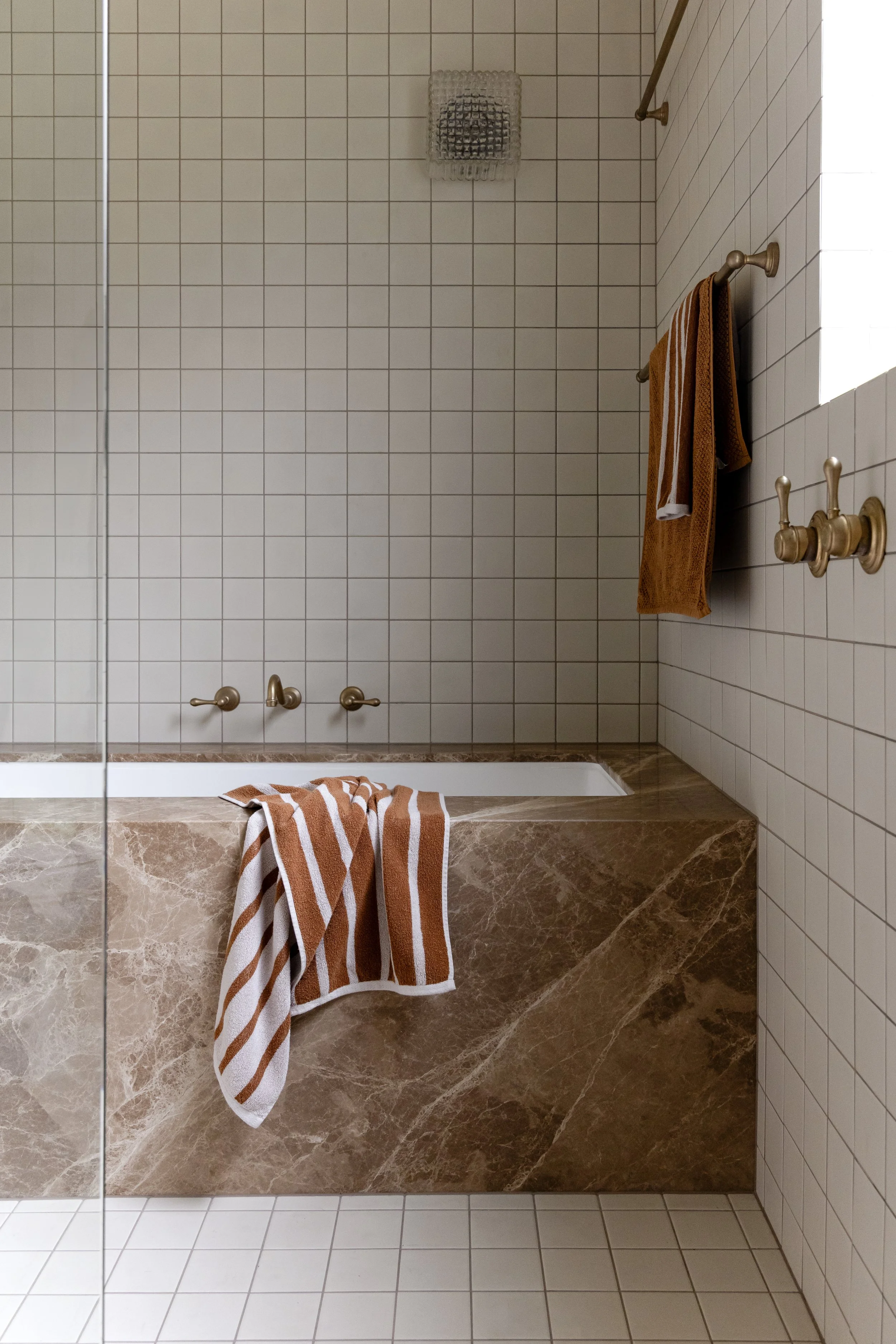 Marble bathtub in bathroom with square tiles and brushed bronze tapware