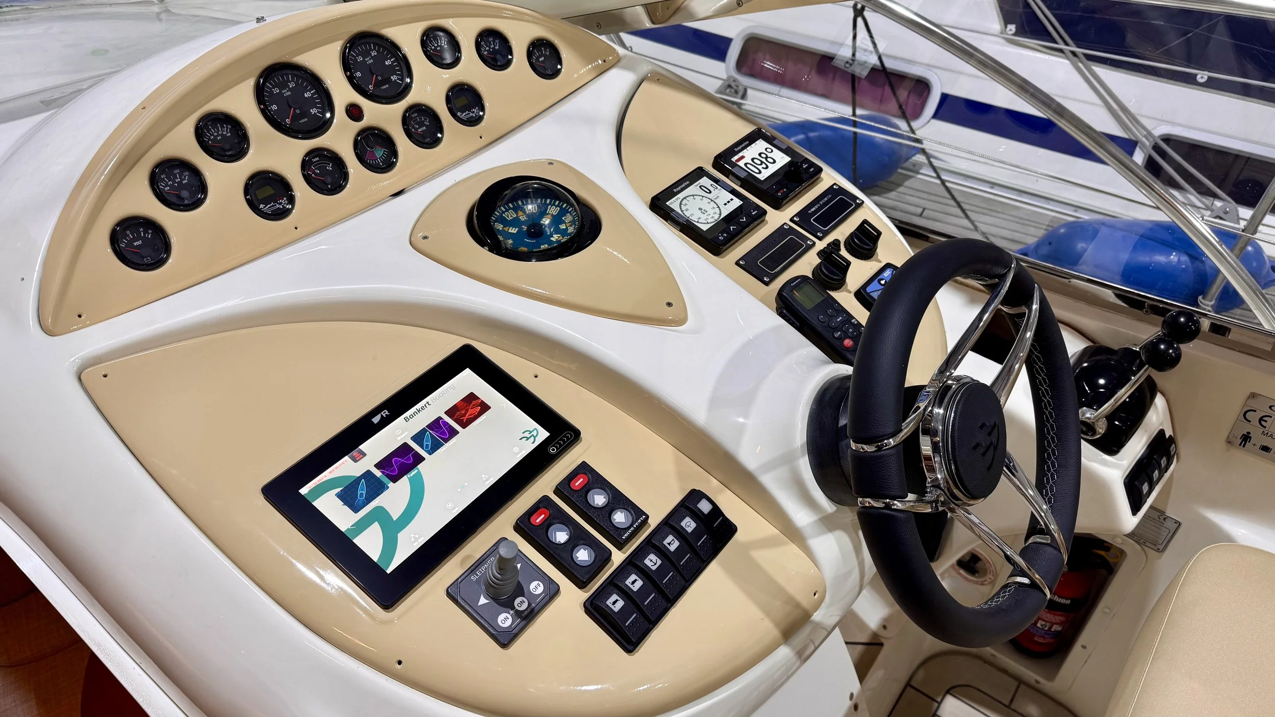 Cockpit of a boat with various gauges, digital displays, and control switches, featuring a black steering wheel with stainless steel accents.