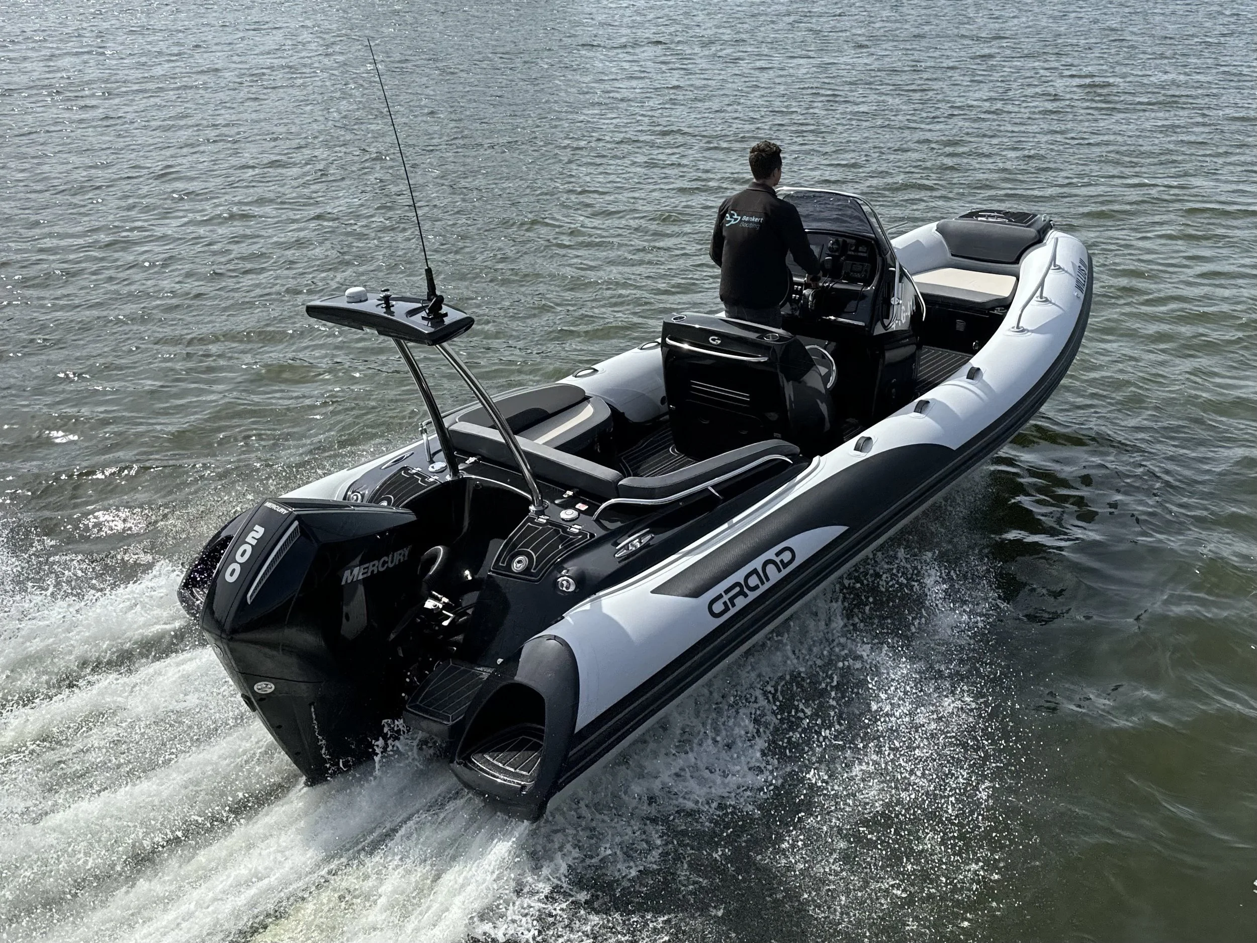 A man is steering a speedboat with a Mercury outboard motor, on a body of water.