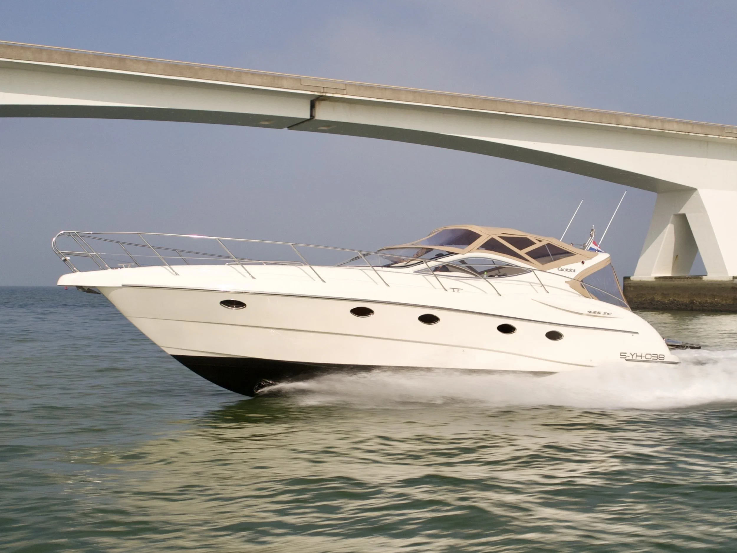 A white yacht boat cruising under a bridge over water.