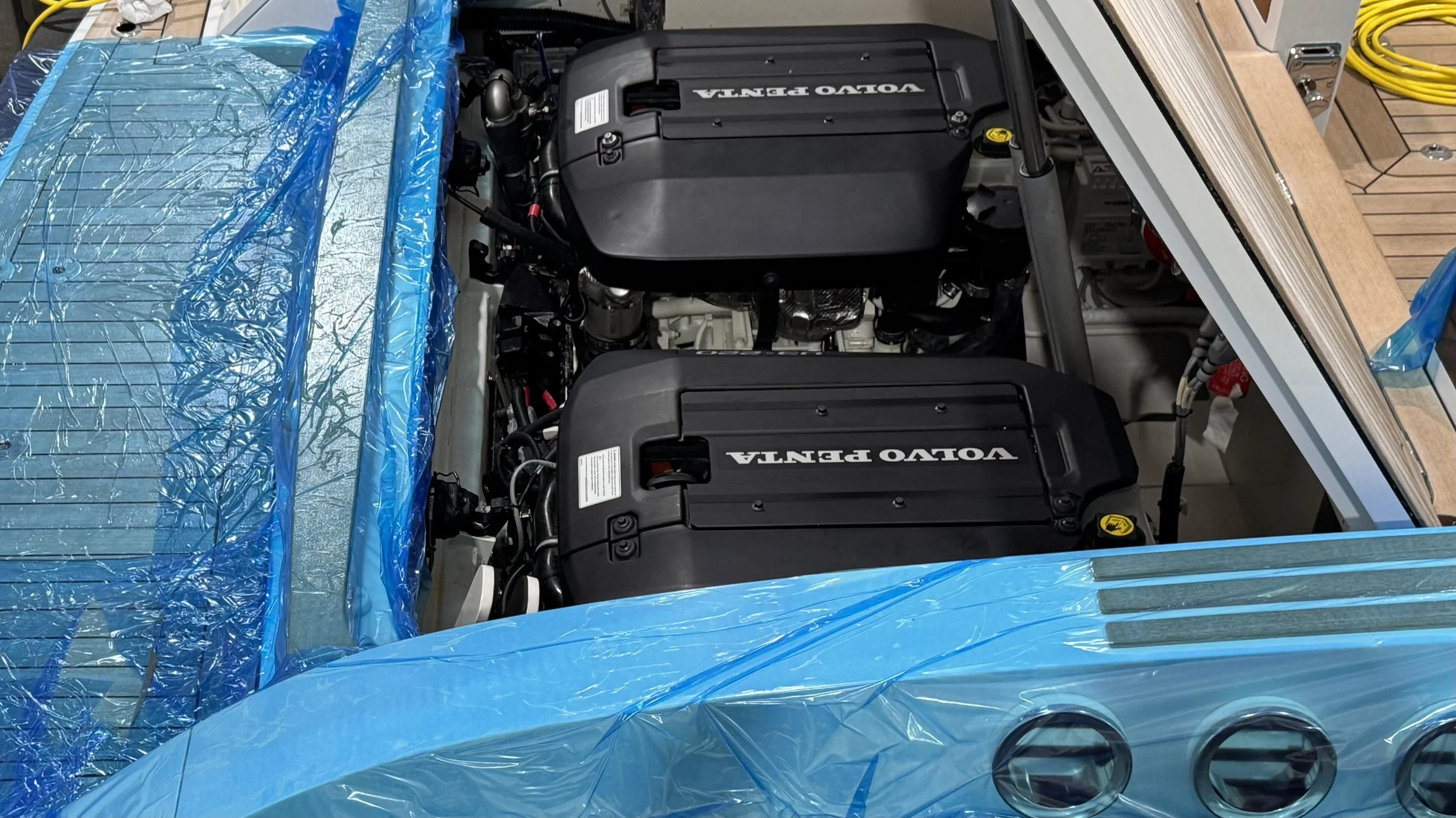 Two Volvo Penta marine engines installed inside a boat with a blue plastic cover partially removed.