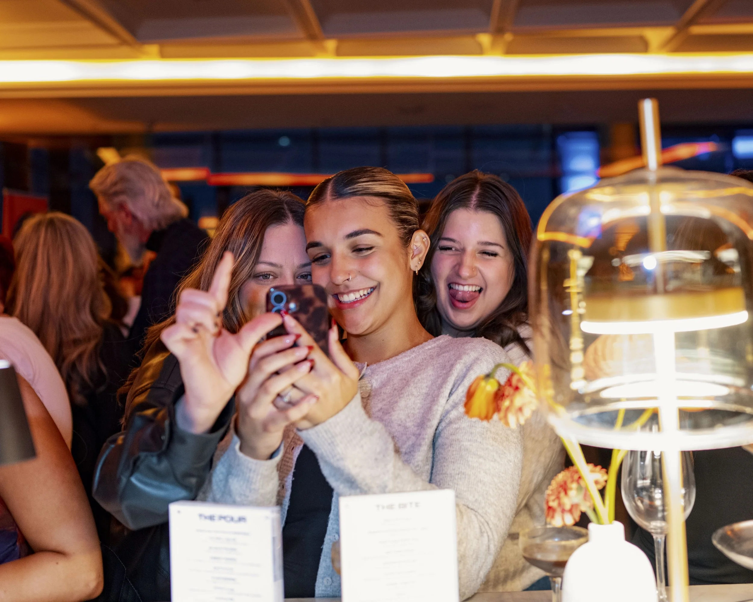 Three women smiling and taking a selfie together at a restaurant or bar