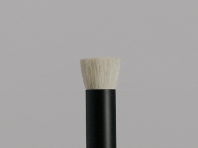 Close-up of a makeup brush with white bristles and a black handle on a light gray background.