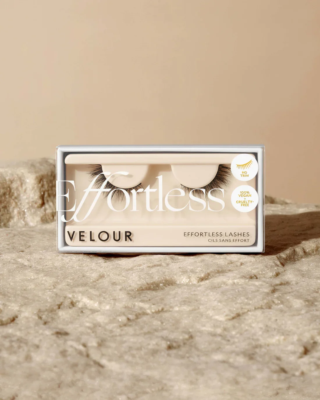 Box of Effortless Velour lashes with black and white packaging, placed on textured beige surface, featuring an illustration of eyelashes and labeling as vegan, cruelty-free, and no trim.