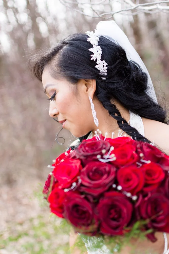 Brunette bride with floral headpiece and long earrings holding a bouquet of red roses outdoors