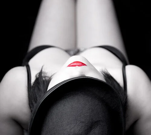 A woman in black lingerie and a wide-brimmed hat, lying on her back with her head tilted back, captured from above.