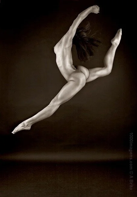 Black and white photo of a person in mid-air, performing a dynamic jump or leap with arms and legs extended.