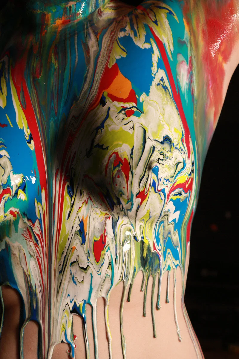 Close-up of a person's torso covered in colorful, swirling paint that is dripping down the skin.
