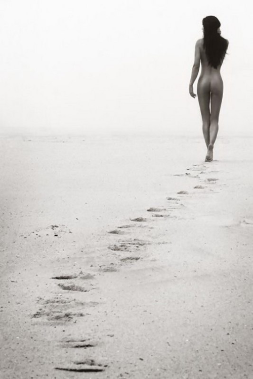 A woman walking alone on a beach, leaving footprints in the sand.