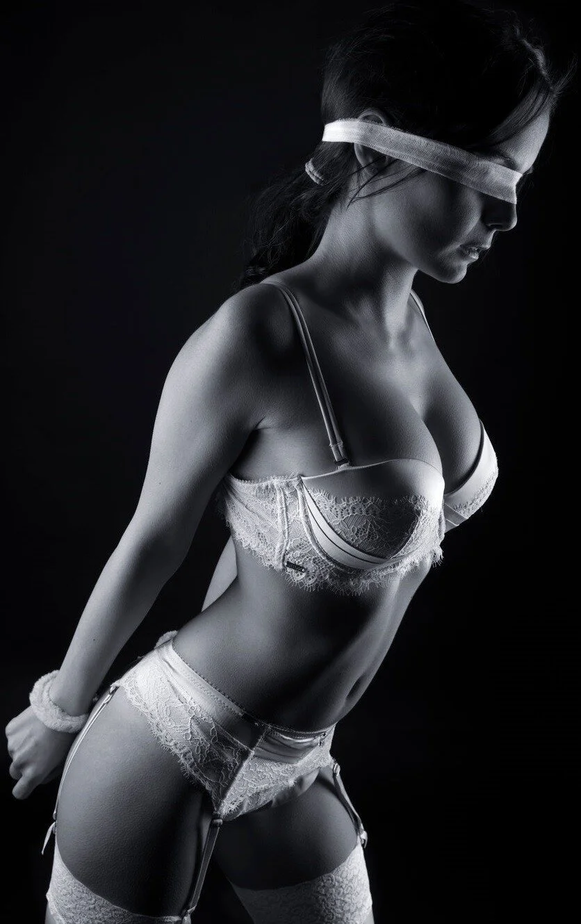A woman with a blindfold in lingerie, posing against a dark background.