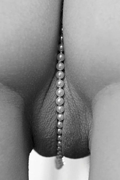 Close-up black-and-white photo of a pearl necklace draped between the thighs.