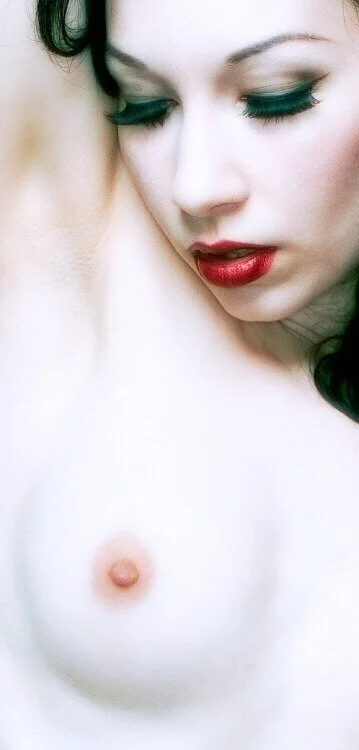 Close-up of a woman with makeup, looking down, with her shoulder and bare chest visible.