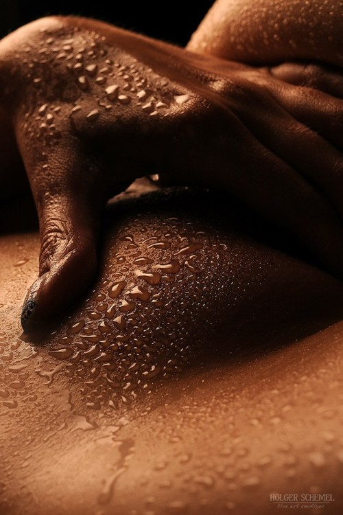 Close-up of a person's hand and chest with water droplets on the skin, illuminated by warm lighting.