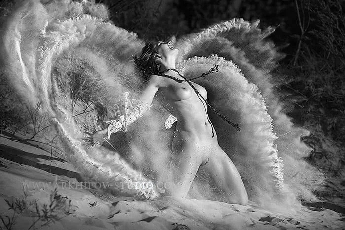 A naked woman surrounded by a large splash of water in a natural outdoor setting.