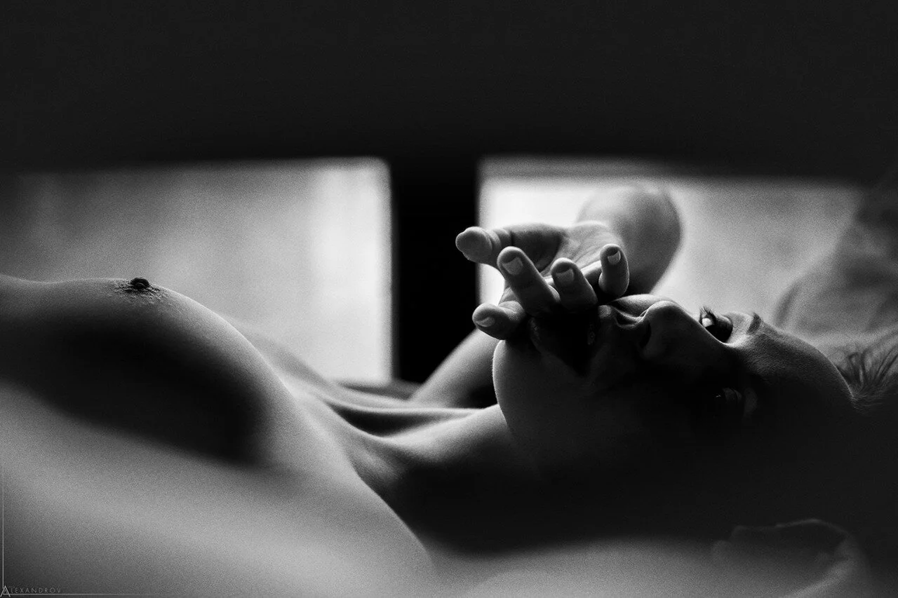 Black and white photo of a person lying down with a focus on their chest and hand, with natural light illuminating the scene.